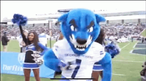 a mascot has his face slightly out, and a cheerleader looks on