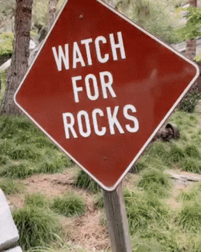 a blue sign warning about rock on the road