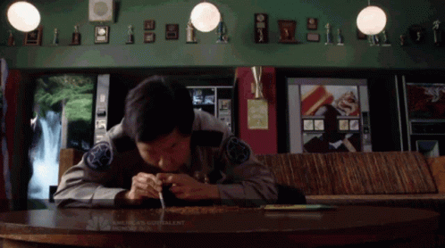 man sitting at table writing while using cellphone