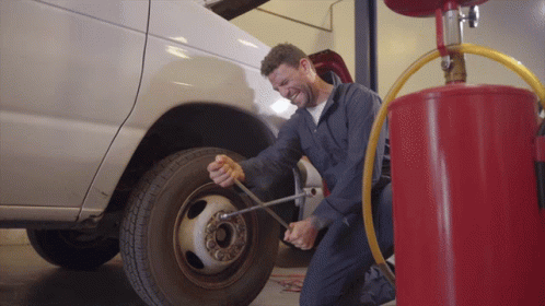 two mechanics work on a vehicle's tire in a garage