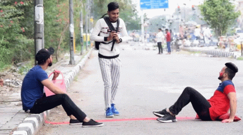 a man is standing on his phone near another man sitting on the ground