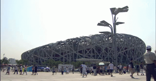 a group of people are gathered in a lot next to an enormous structure