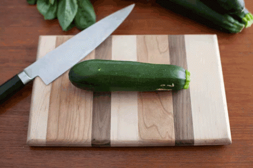 green cucumbers, basil and knife on  board