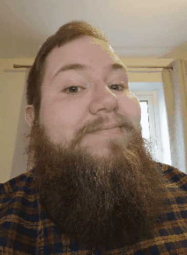 man with long dark beard in checkered shirt and window