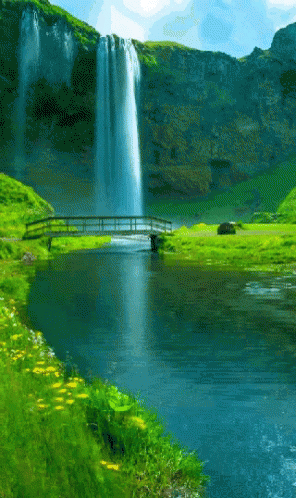 a waterfall with green grass and a bridge