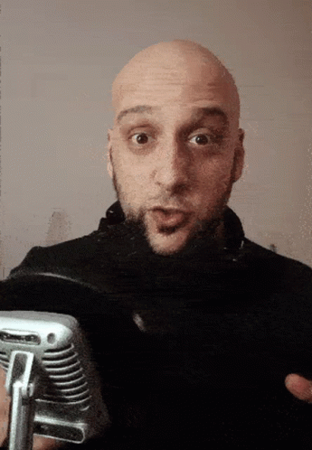 a bald man holding a microphone looking into the camera