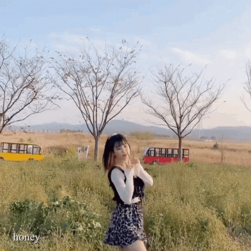 a woman stands in tall grass near a bunch of buses