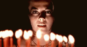a woman with pearls around her neck standing in front of candles