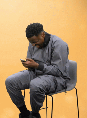 a man sitting down on a chair and looking at his phone