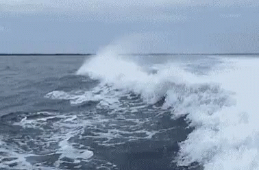 waves crashing up against the ship, with a person sitting on the back of a boat
