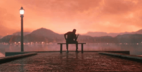 person sitting on bench looking out to a lake at night