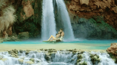 two people sitting on a rock near a waterfall