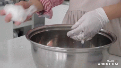 a woman in blue gloves puts soing in a bowl