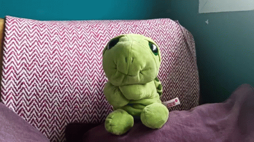 a stuffed green dinosaur is sitting on a bed