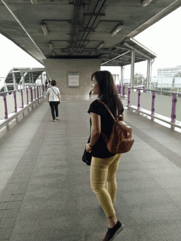 two people walking across a bridge with a backpack on their back