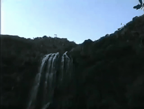 two people are jumping off the side of a waterfall