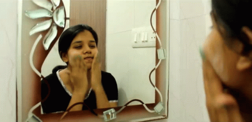 a woman brushes her teeth while looking in a bathroom mirror
