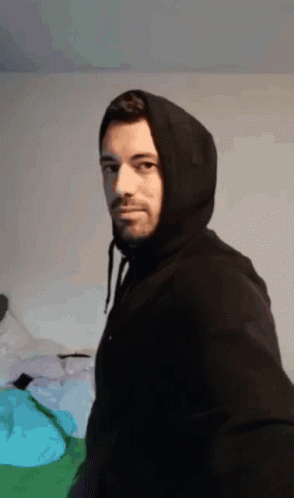 man in a hooded jacket standing in front of a bed