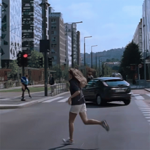 a skateboarder crossing a city street with a car approaching