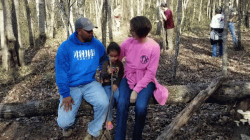 people are standing in the woods, one man is holding a young child