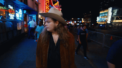 a woman with long hair in a cowboy hat is standing on the sidewalk