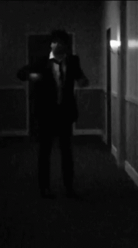 a man in black suit and tie walking into dark room