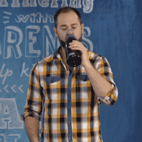 a man wearing a flannel shirt is singing in front of an abstract background with writing