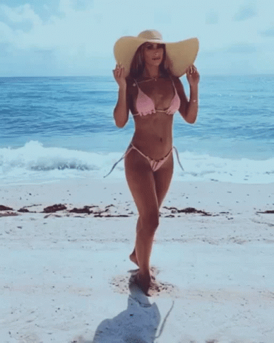 a young woman wearing a bikini walks on the beach