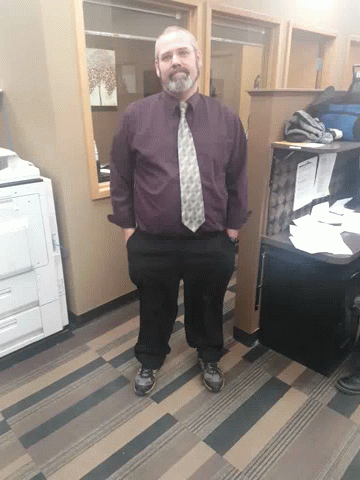 man in purple shirt and tie standing inside of a cubicle