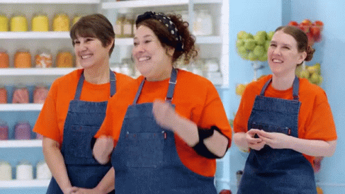 three women in brown aprons stand with arms folded