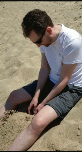 a man sitting in the sand while holding his foot on the ground