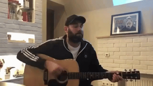 a man holding an acoustic guitar in a kitchen