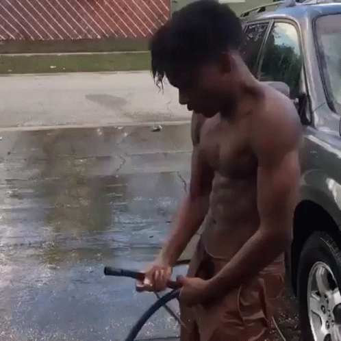 a shirtless man holding a gas pump next to a parked vehicle