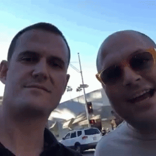 two males wearing sunglasses standing together in front of a street