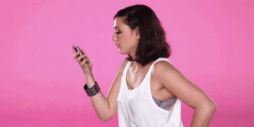 a woman wearing a white tank top is holding up a cell phone