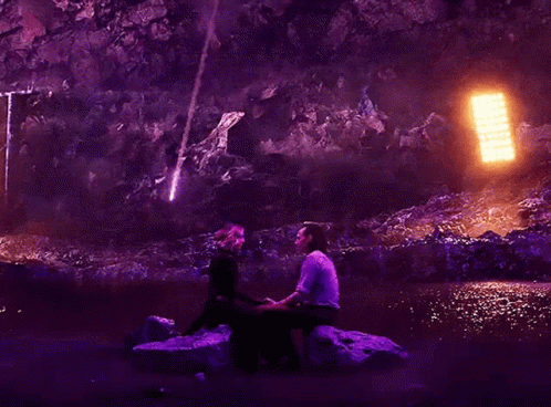 two people are sitting near a waterfall on the rocks