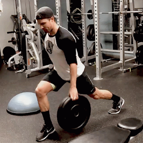 man at the gym working out with one leg in a squat position while a medicine ball sits in the background