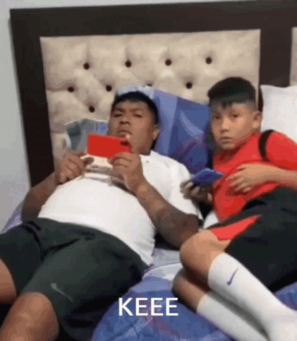 two men in bed with cell phones while they look at each other