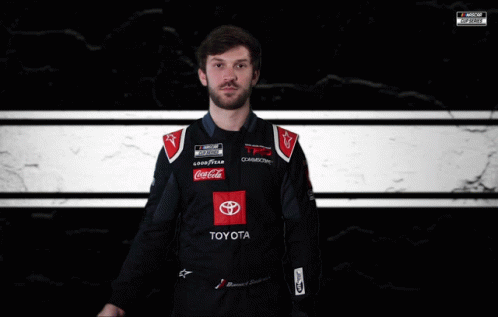 a man wearing a racing suit in front of a black wall