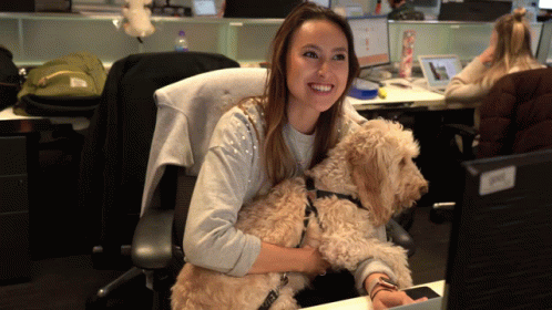 a woman holding a dog in her lap sitting on a chair in an office