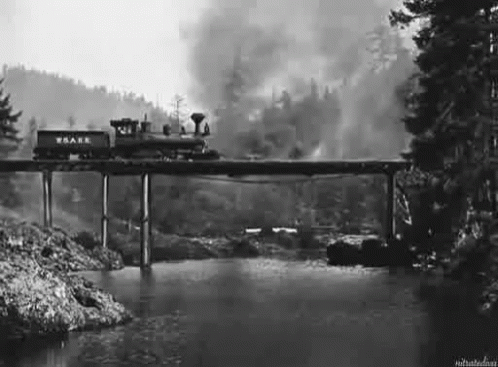 a black and white image shows the train crossing a bridge that is on fire