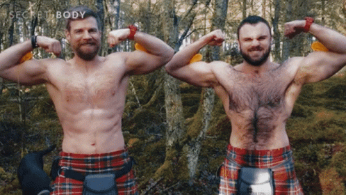 two men wearing kilts standing in a forest