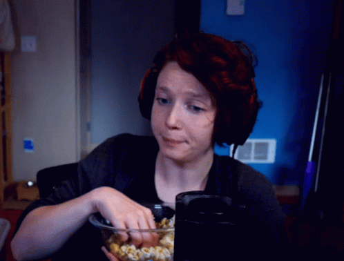 a woman with blue makeup is eating popcorn and drinking from a glass