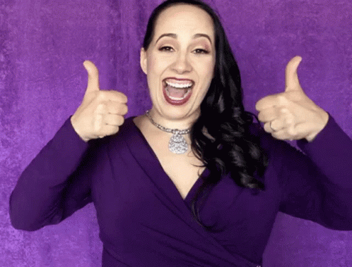 a woman posing in front of a pink background holding up two thumbs