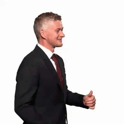 a man in a suit standing with his hands folded and making gestures