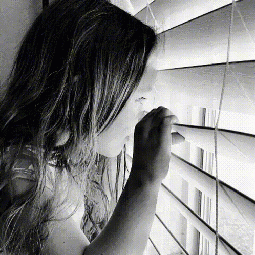 a little girl looking through a blinds in the shade