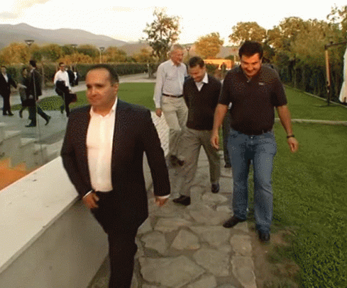 a man wearing a black suit and white shirt walks down a brick sidewalk with other men in dark colored suits