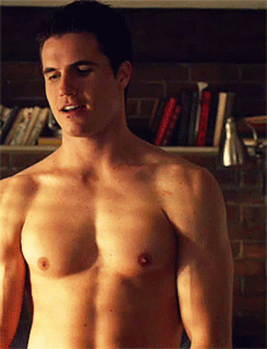 a shirtless young man standing in front of a bookshelf