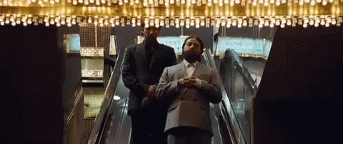 a man walks down a escalator next to a woman in a suit