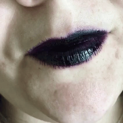 a woman with a purple lipstick and makeup looking straight at the camera